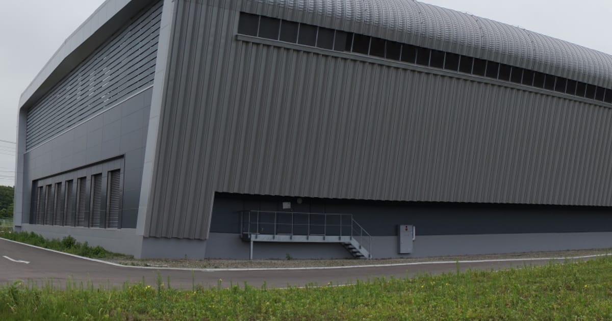 Sakura Internet’s Ishikari data centre in Hokkaido: a long grey building with a curved roof, beside a lawn.